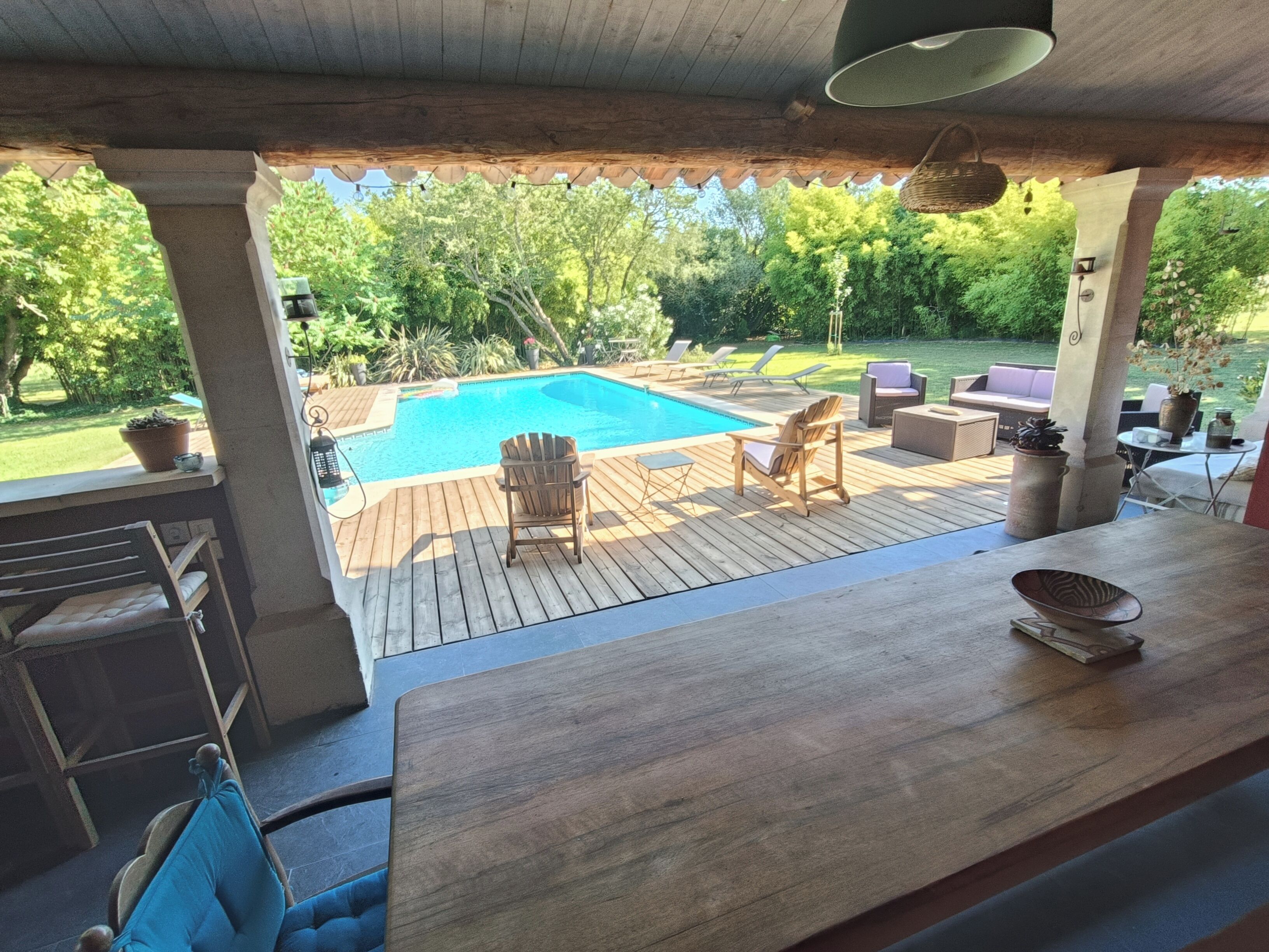 A wooden deck with a pool, outdoor furniture, and a view of a lush garden.