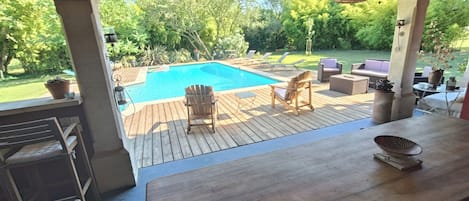 Una terraza de madera con piscina, mobiliario exterior y vistas a un jardín exuberante.