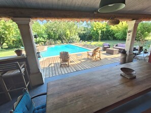 Eine Holzterrasse mit Pool, Gartenmöbeln und Blick auf einen üppigen Garten.