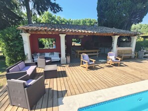 Ein überdachter Außenbereich mit Pool, Holzterrasse, Korbmöbeln und Grillmöglichkeit.