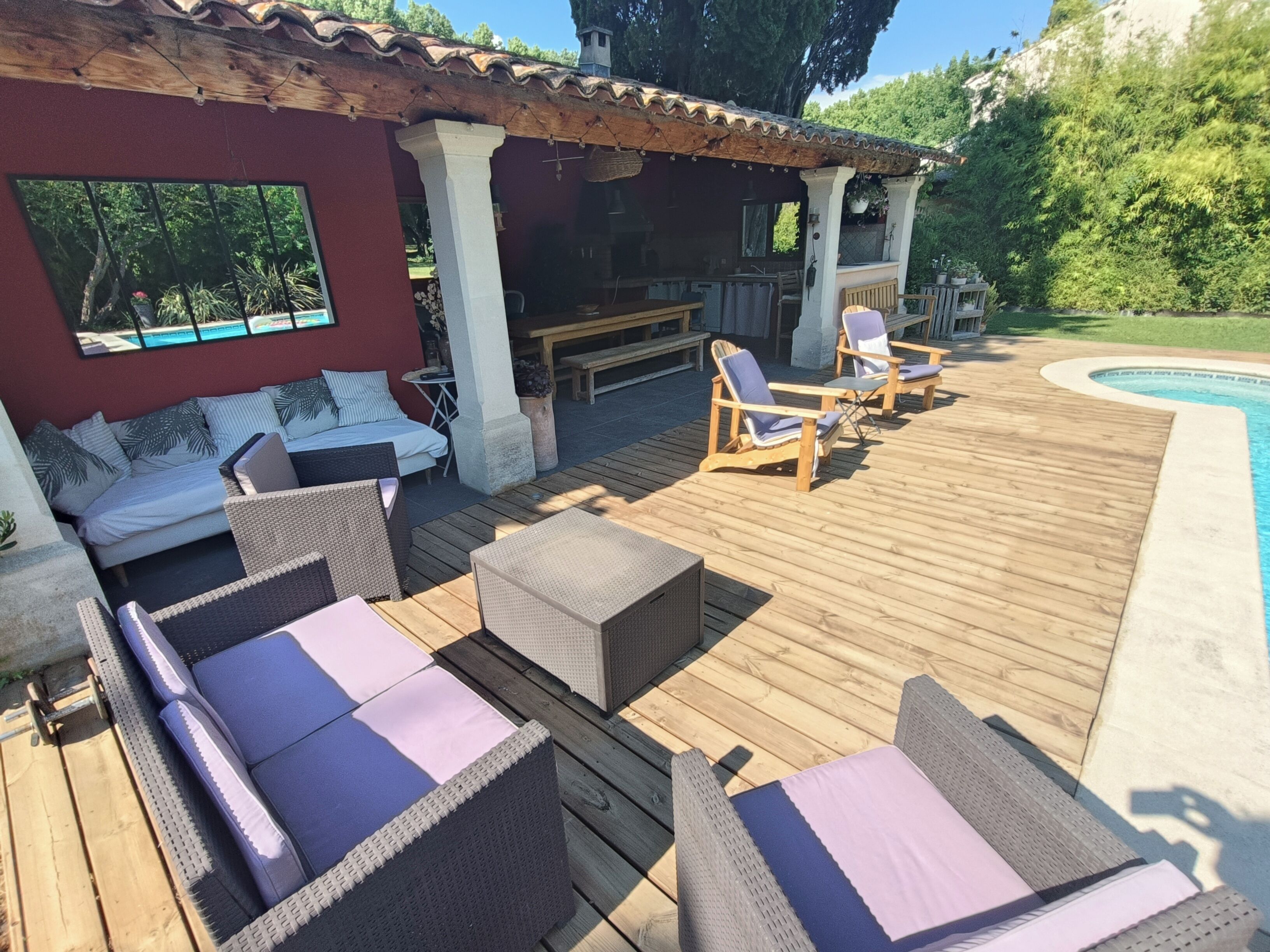 Une terrasse en bois avec des meubles en osier, une piscine et un espace couvert comprenant une table et des chaises.