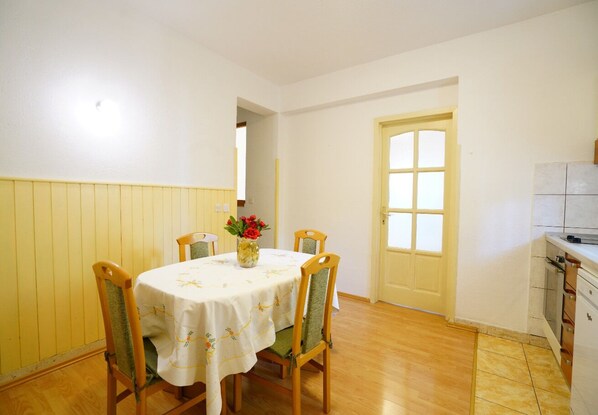 A dining area with a round table covered by a white tablecloth, surrounded by wooden chairs with green cushions. A vase with flowers is placed on the table. - Apps Maria: place to spend holidays with friends & family in Split (Croatia) (Podstrana)