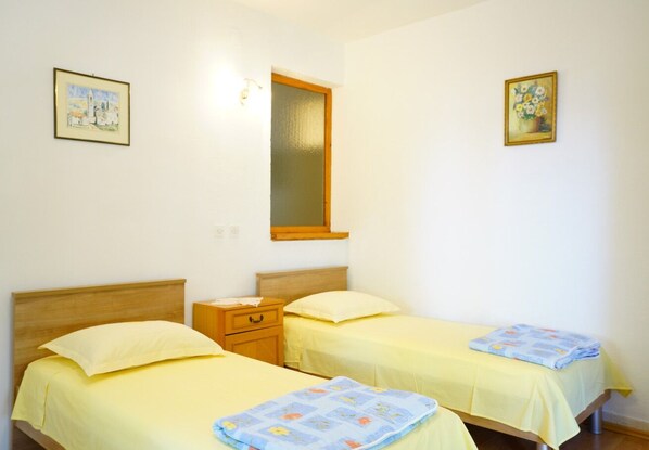 Une chambre avec deux lits simples, une table de chevet en bois, un miroir et deux tableaux encadrés accrochés aux murs.