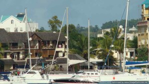 Un port de plaisance où sont amarrés des bateaux, entouré de bâtiments aux toits de chaume et de quelques constructions modernes.