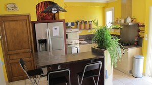 A compact kitchen with a refrigerator, oven, and a sink. There are two bar stools and a potted plant.