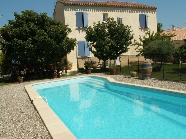 A swimming pool with a tiled edge, surrounded by a gravel area and potted plants.