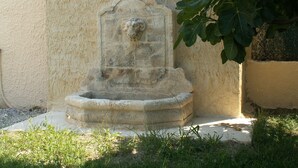 A stone fountain with a carved figure, surrounded by grass and a wall.