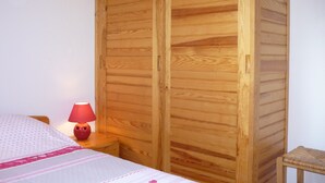 A bedroom with a wooden wardrobe, a bedside table with a lamp, and a bed with a patterned bedspread.