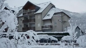 A multi-story building with balconies, surrounded by snow-covered trees and a mountain in the background.