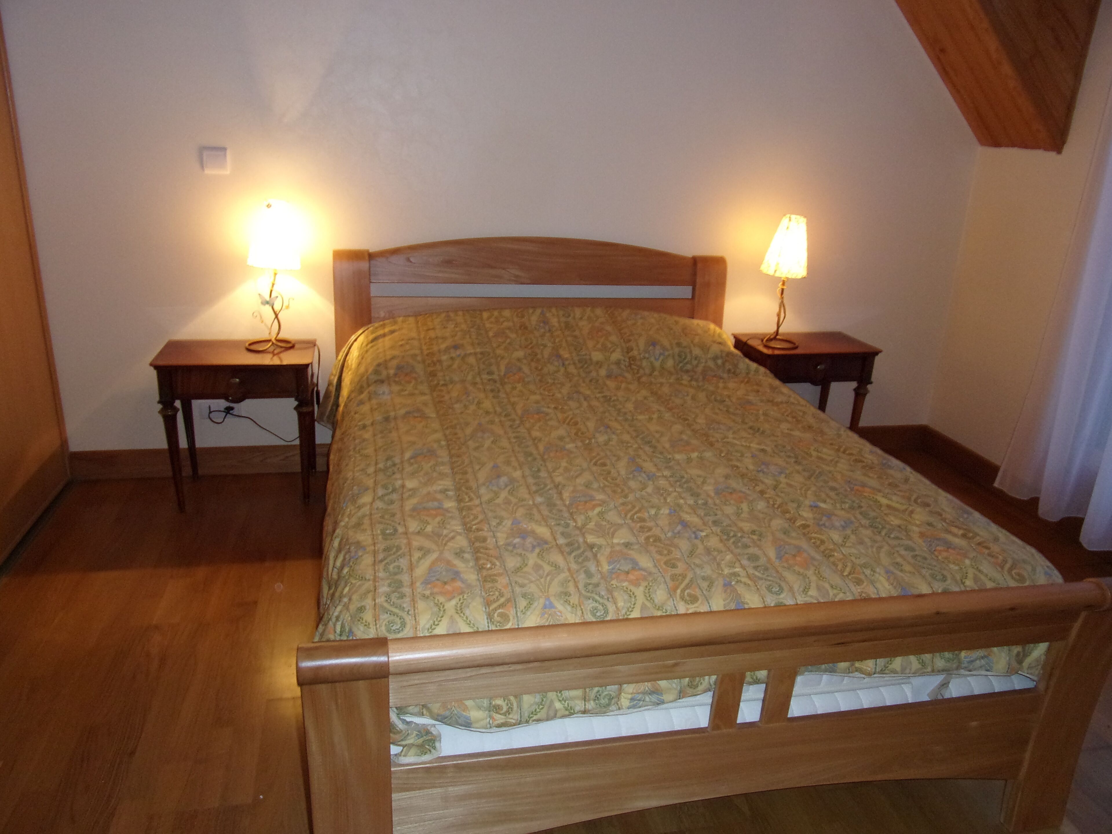 Ein Schlafzimmer mit einem hölzernen Bett, zwei Nachttischen mit Lampen und einer gemusterten Tagesdecke.