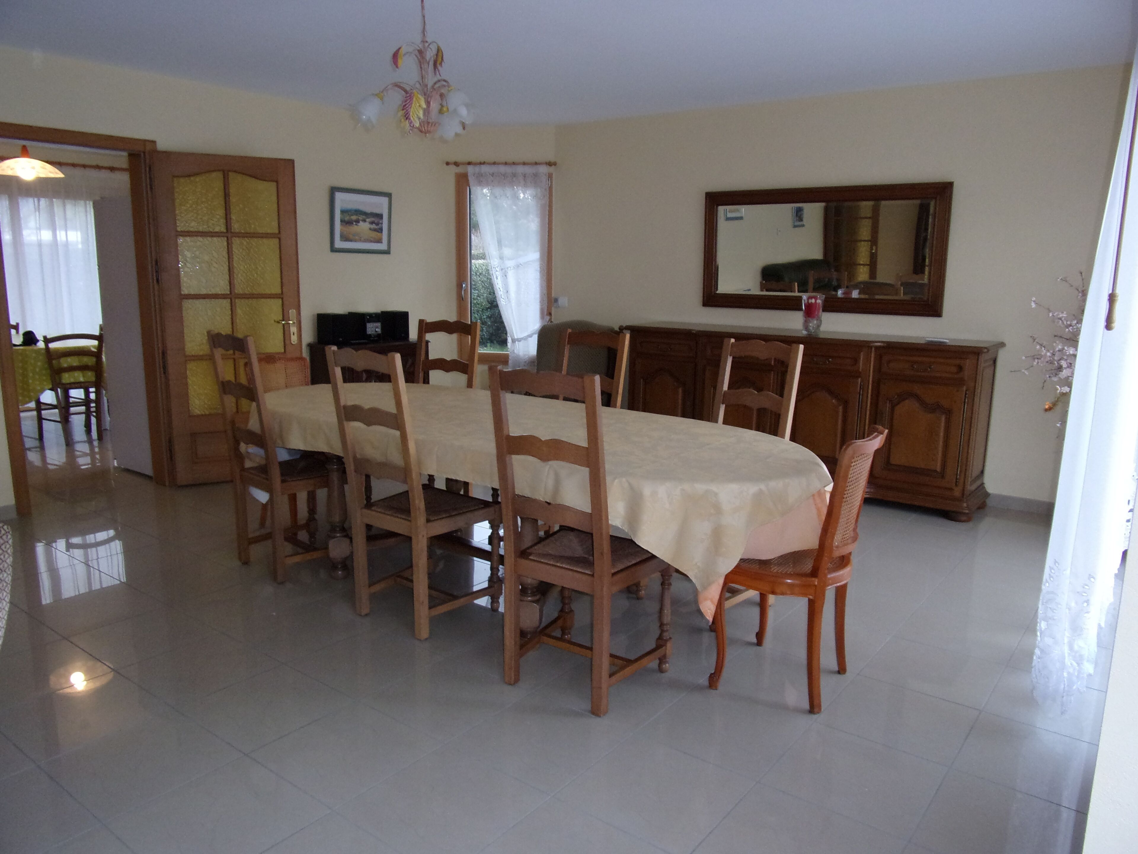 Uma sala de jantar com uma mesa comprida, cadeiras de madeira, um candelabro, uma televisão e um armário.