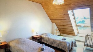 Un dormitorio con dos camas, techo de madera y un ventanal grande.