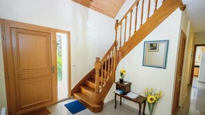 Una escalera de madera con barandilla, una puerta de madera, una pequeña mesa con un florero y un cuadro en la pared.