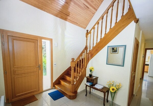 A wooden staircase with a handrail, a wooden door, a small table with a vase of flowers, and a framed picture on the wall. - House for 12 persons close to the beach with a warmed up pool (Concarneau)
