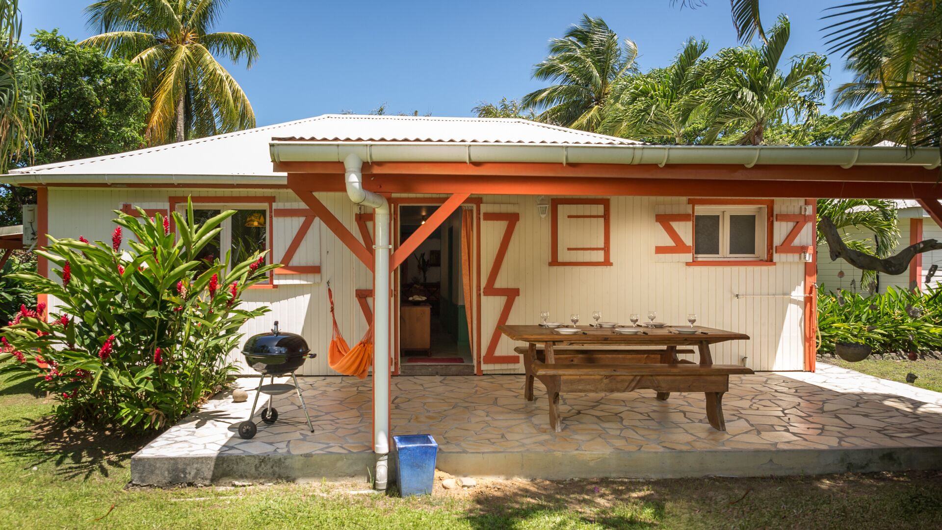 A small house with a covered patio, a barbecue grill, and a dining table set for four.