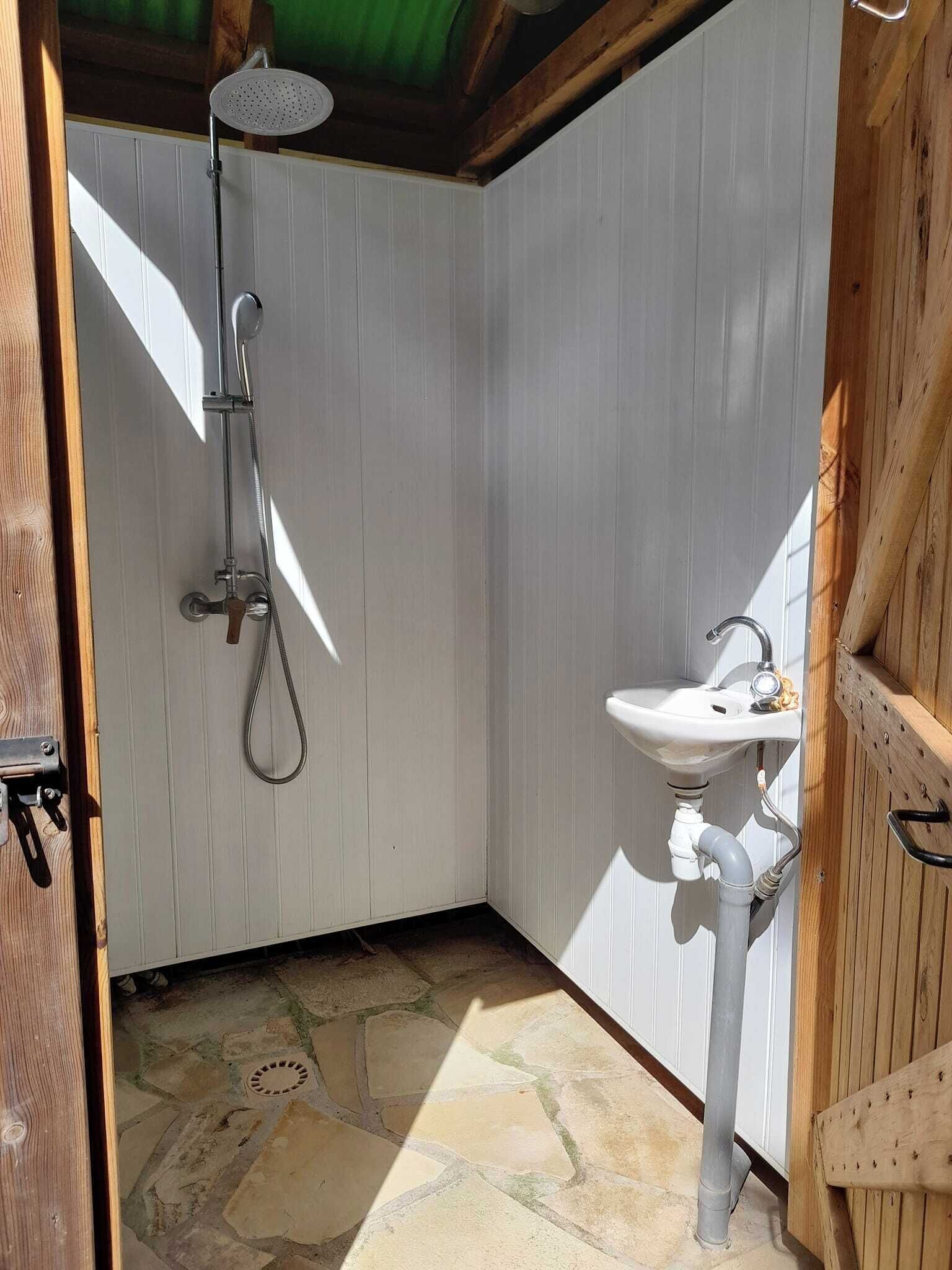 Ein kleines Badezimmer mit Dusche, Waschbecken und einer Holztür.