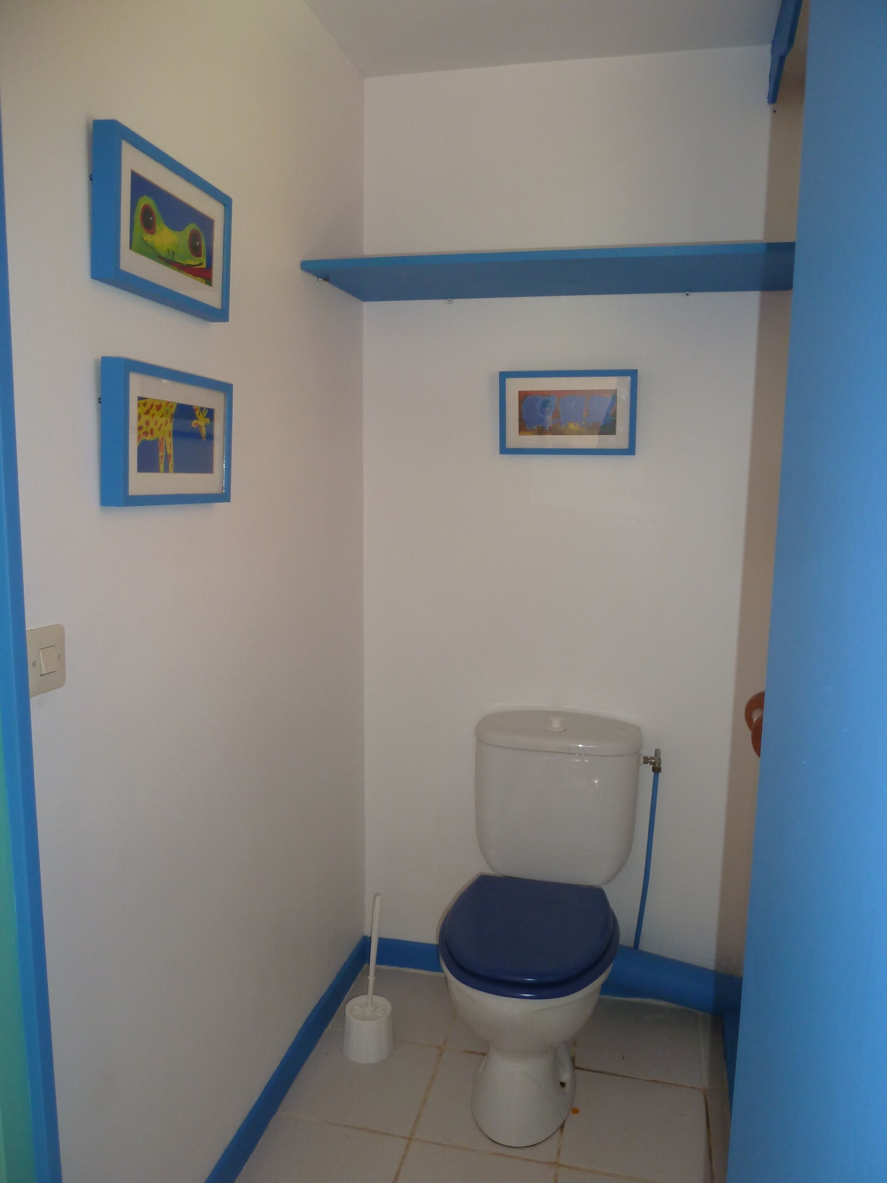 A small bathroom with a toilet, a bidet, and three framed pictures on the wall.