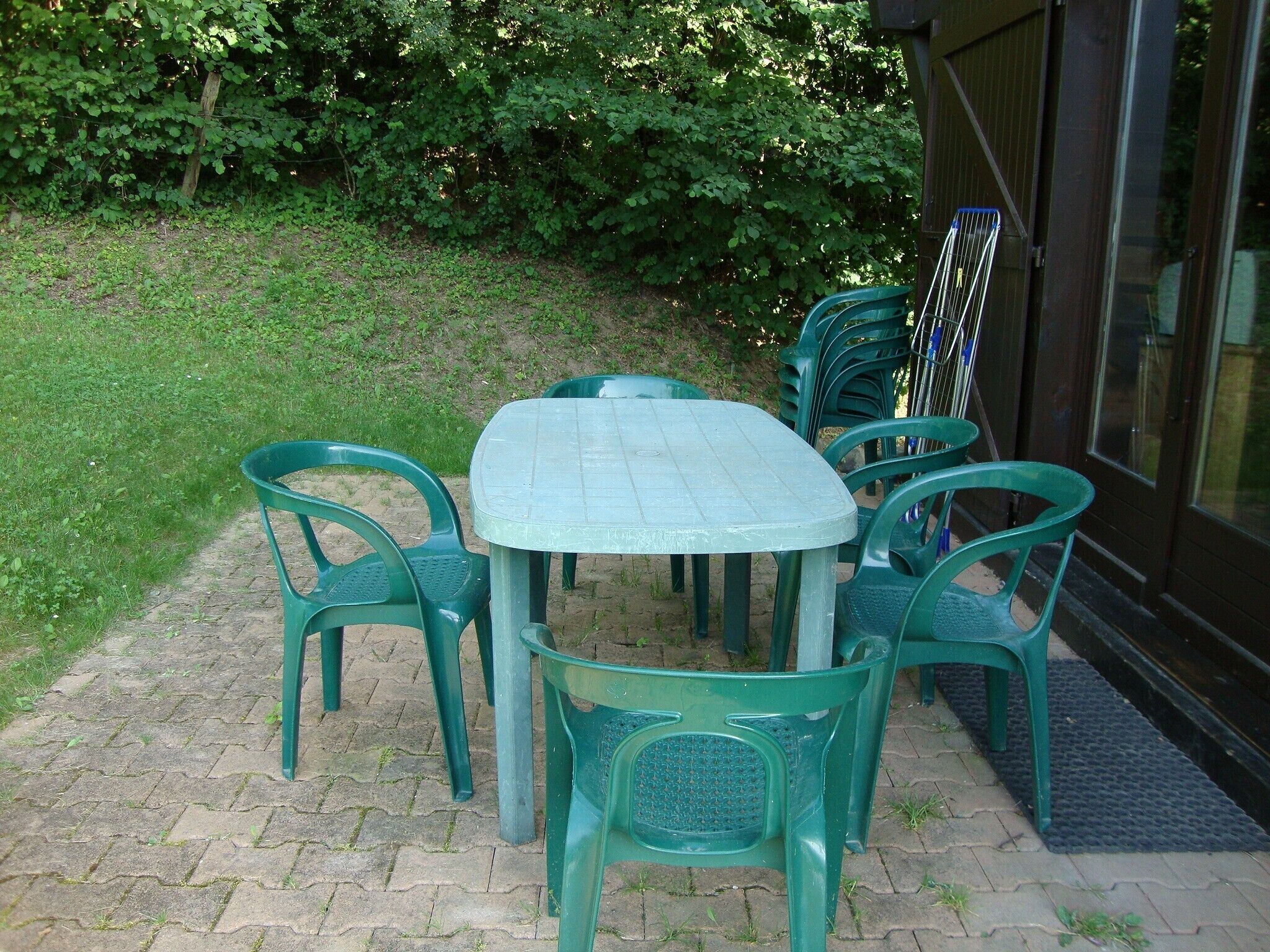 An outdoor patio with a round table and six green plastic chairs.