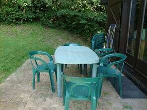 Un patio al aire libre con una mesa redonda y seis sillas de plástico verde.