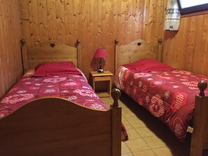 Una habitación con dos camas de madera, cada una con cabecera y piecera, y una mesita de noche con lámpara.