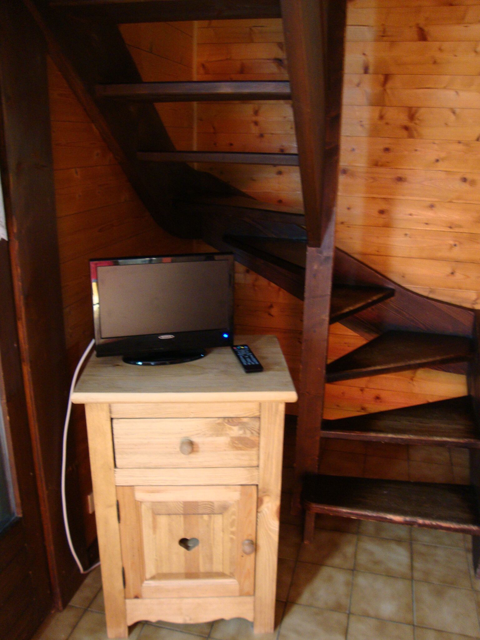 Un bureau en bois, sur lequel se trouvent un ordinateur portable et une télécommande, est placé à côté d’un escalier en bois.