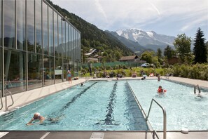 Una piscina con agua cristalina, rodeada por un edificio de vidrio, y montañas al fondo.