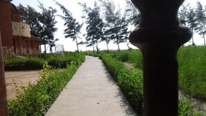 A concrete pathway flanked by green hedges and trees, leading towards a stone building with a balcony. - Between sea and lagoon "KEUR OCEAN" A PARADISE (Nianing)