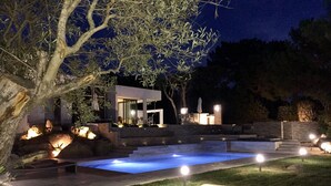 Zona de piscina exterior moderna amb una piscina blava cristal·lina, envoltada d'escales de pedra i un pati ben il·luminat.