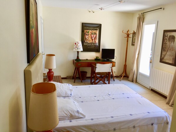 A hotel room with a bed, desk, chair, lamp, and a poster on the wall. - A bright and spacious guest room with a separate entrance. (Carry-Le-Rouet)