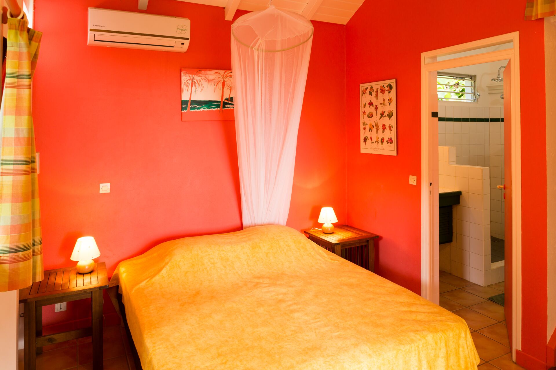 Een kamer met een bed, twee nachtkastjes met lampen, een klamboe, een airconditioner en een deur naar een andere kamer.