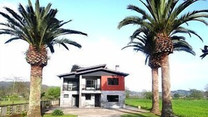 A modern two-story house with a red and white exterior, surrounded by palm trees and a green field.