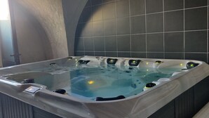 Un jacuzzi con panel de control, rodeado de baldosas oscuras y una pared de piedra.