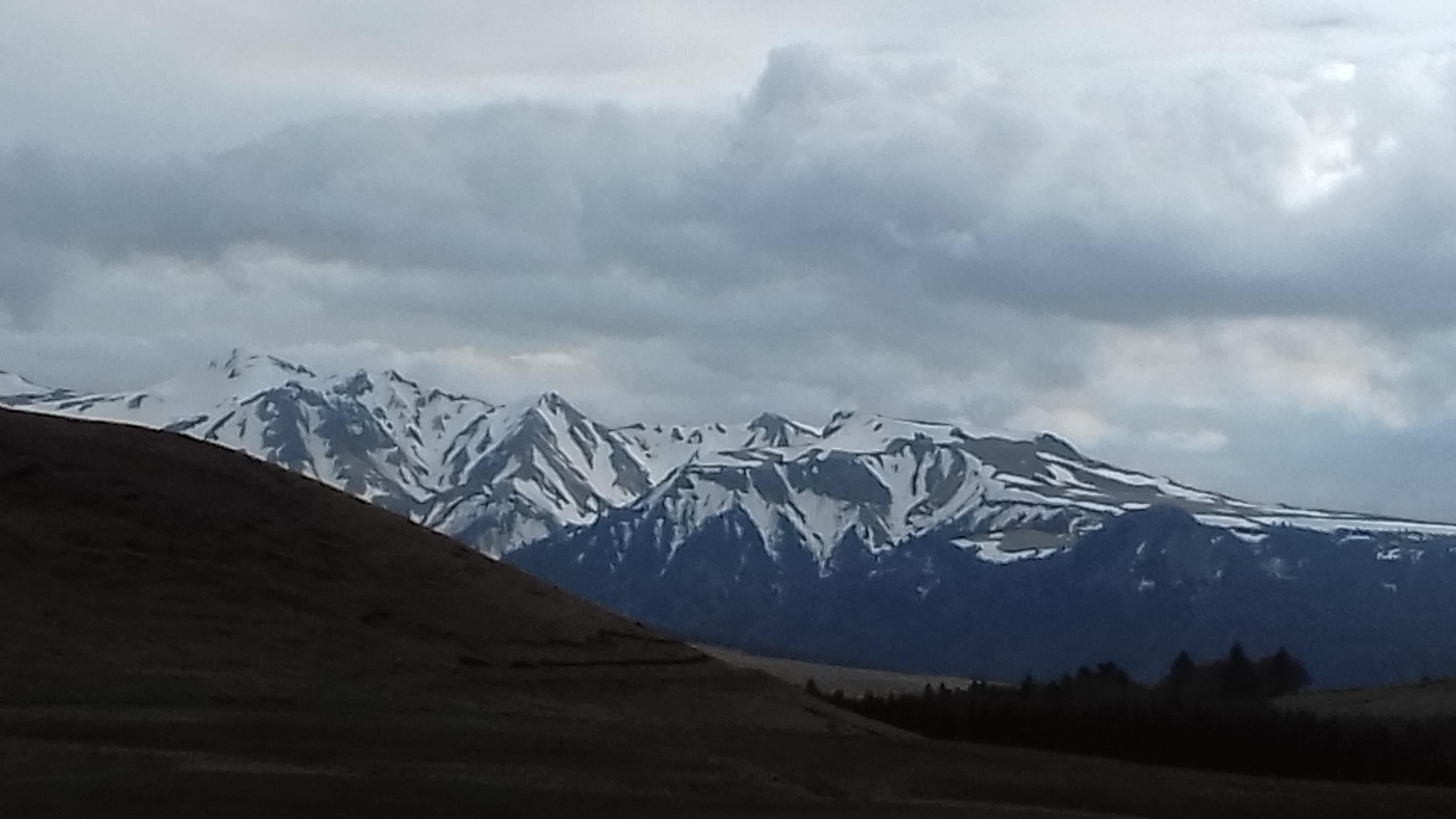 Paesaggio montuoso con cime innevate e cielo nuvoloso.