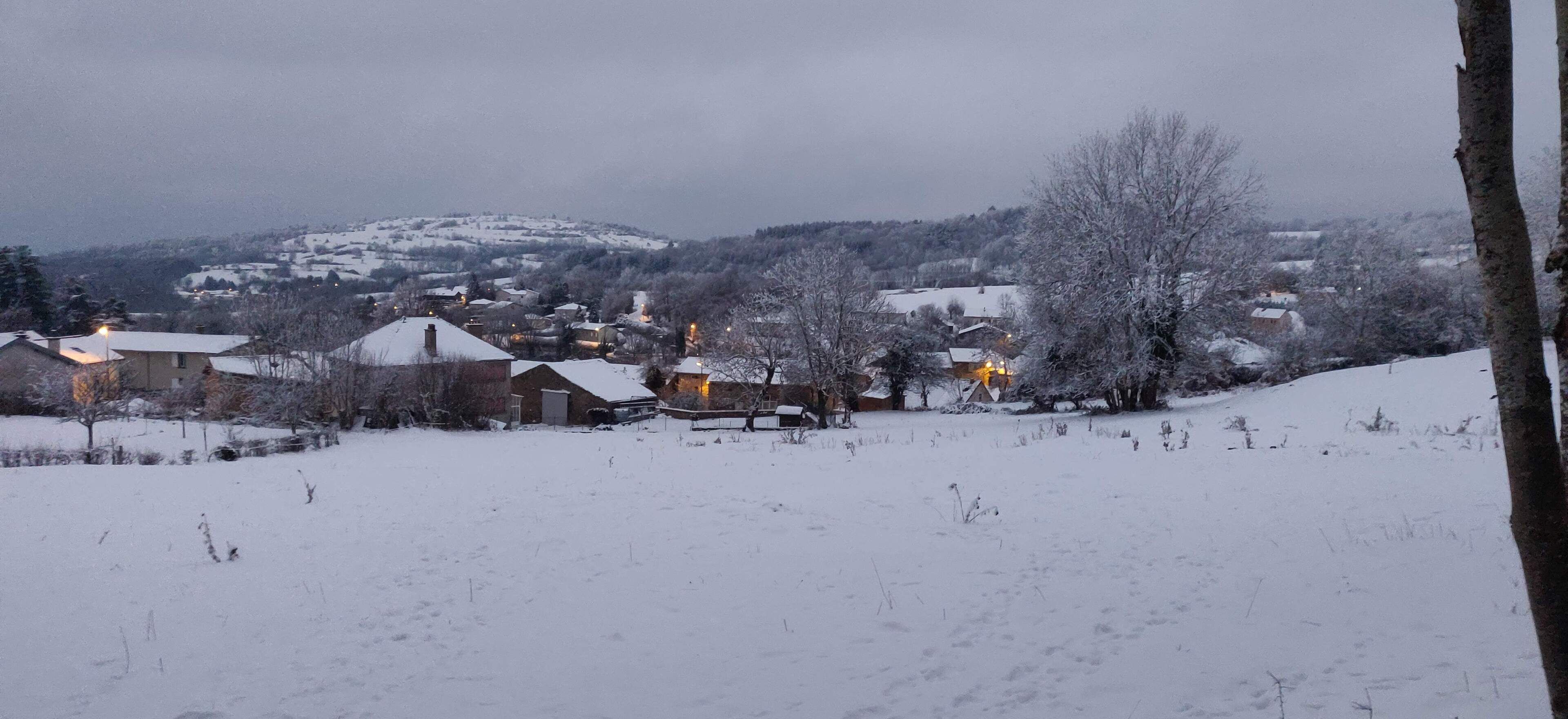 Un village enneigé, avec des maisons et une colline en arrière-plan.
