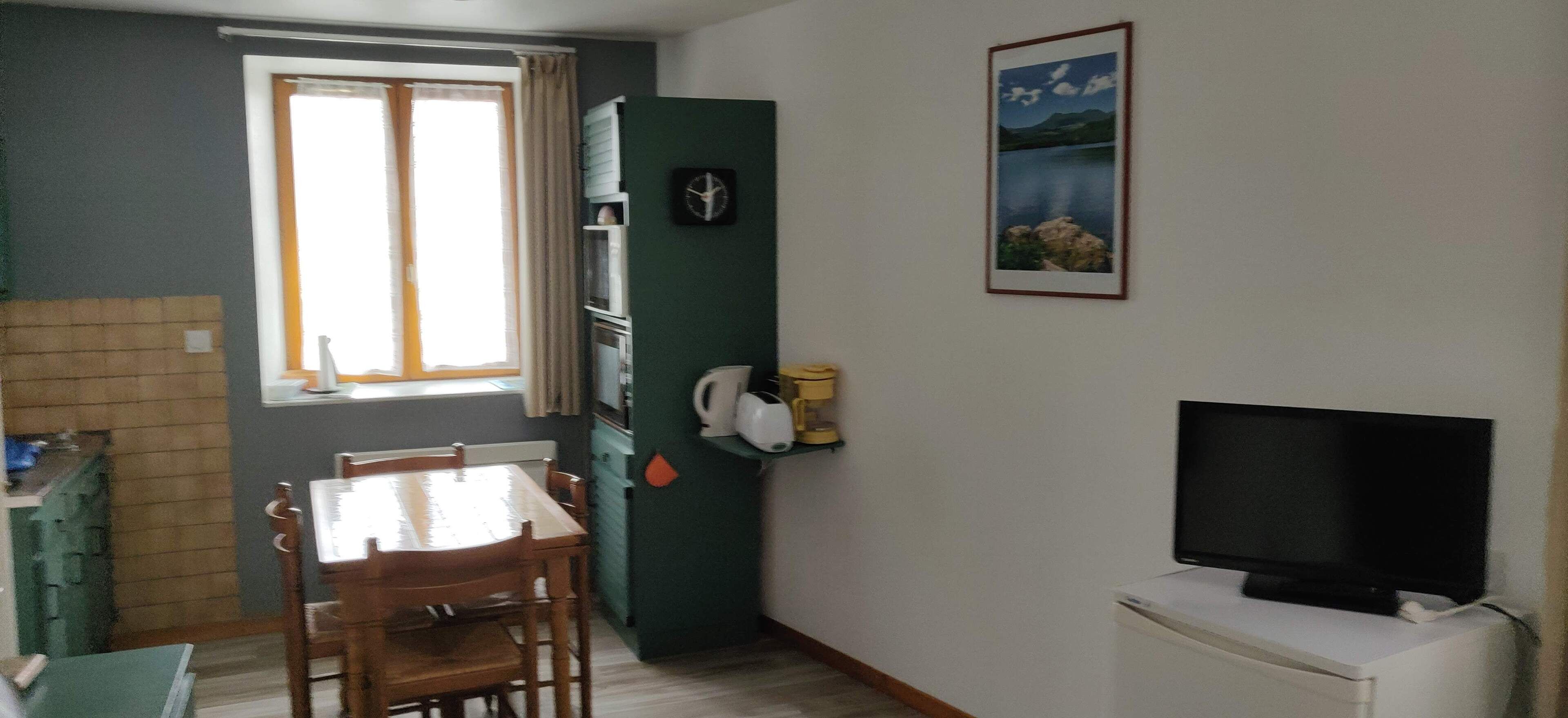 Een kleine keuken met een eethoek, een televisie en een raam met gordijnen.