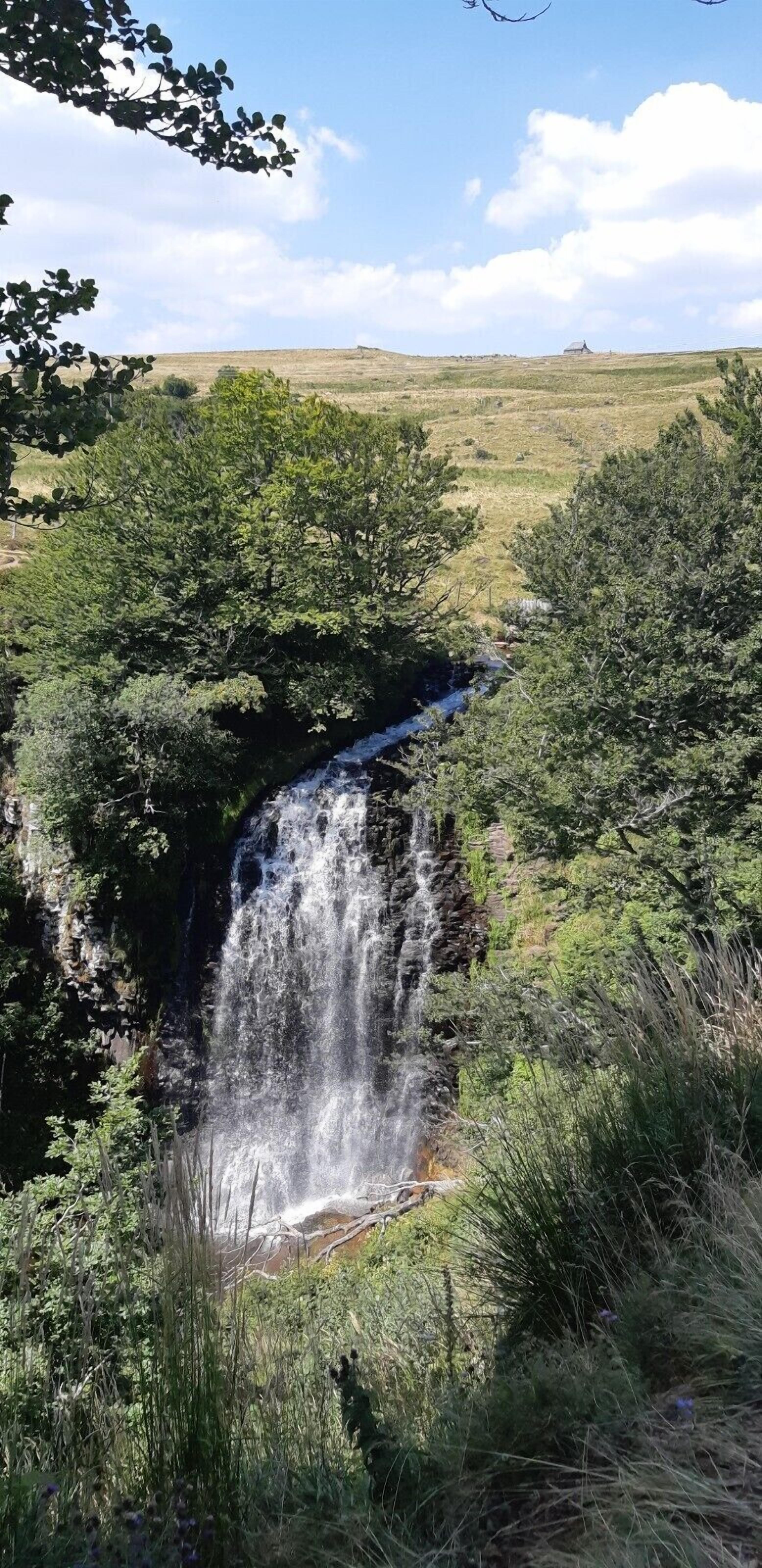 A waterfall surrounded by lush greenery and a clear sky.