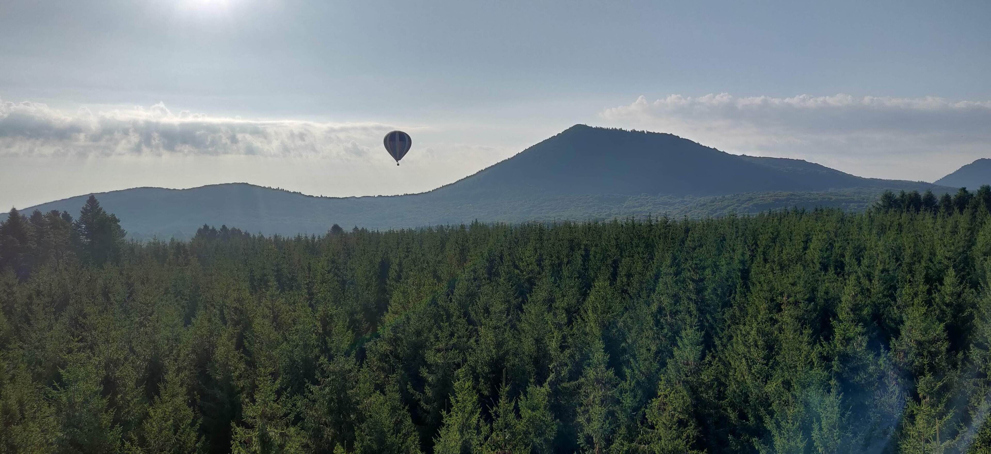 Un globo aerostático sobre un área boscosa con una montaña al fondo.