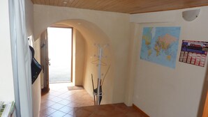 Un pasillo con suelo de baldosas, un perchero, un mapa en la pared y una puerta que da a otra habitación.