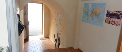 Un pasillo con suelo de baldosas, un perchero, un mapa en la pared y una puerta que da a otra habitación.