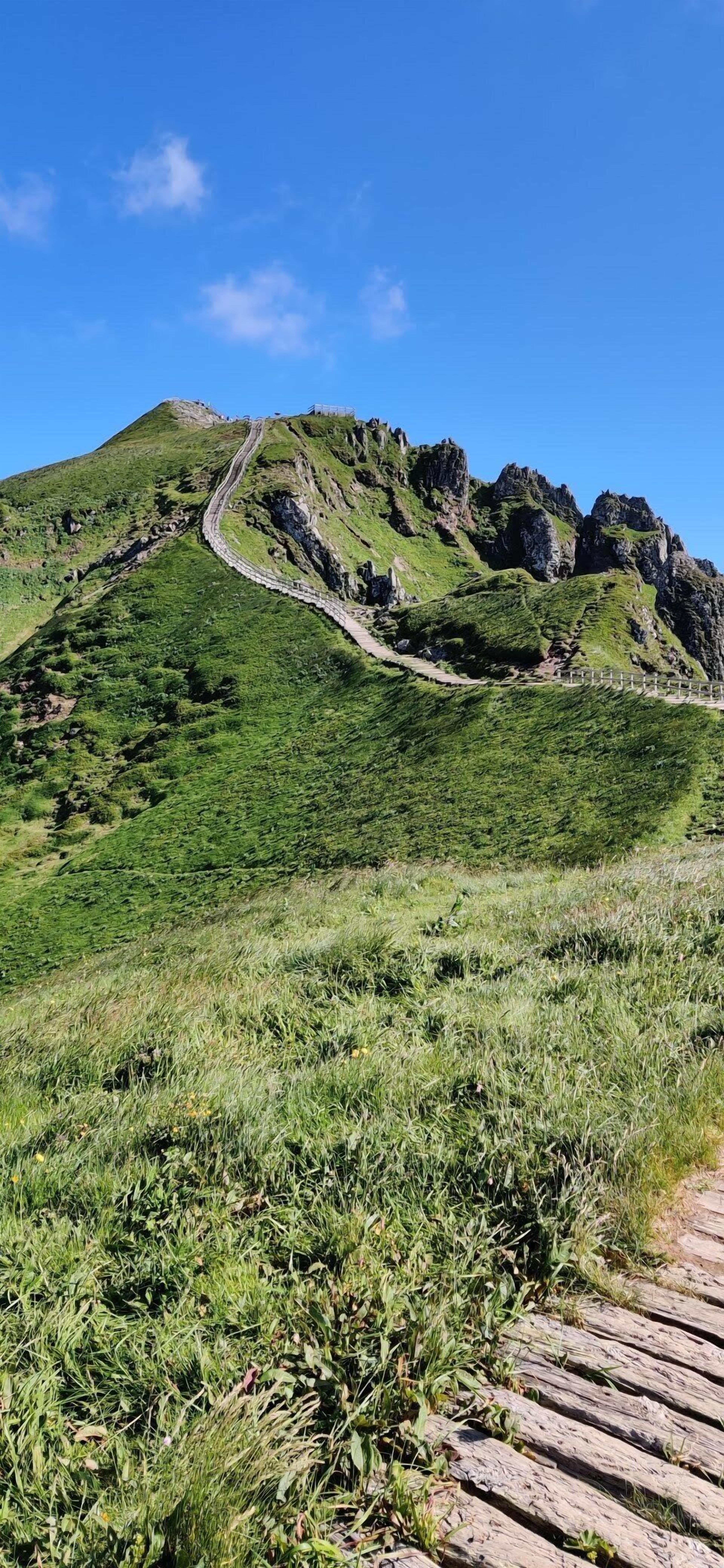 Ein Bergpfad mit einem Holzsteg, der zu einem felsigen Gipfel führt.