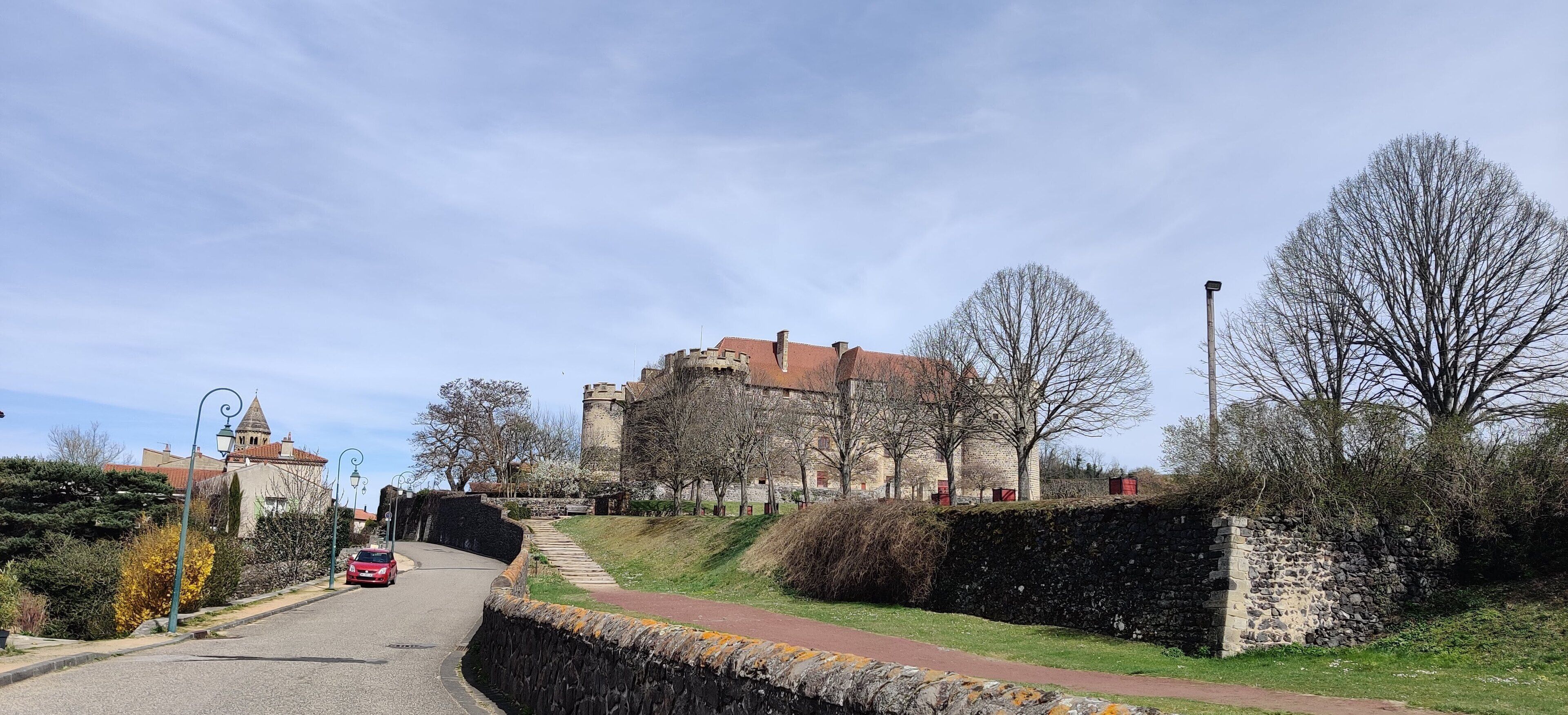 A castle-like building with a stone wall and a paved road leading to it.