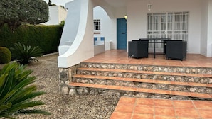 A covered outdoor seating area with a table and chairs, a blue door, and a white wall. - House / Villa - Coma-ruga (Coma-Ruga)