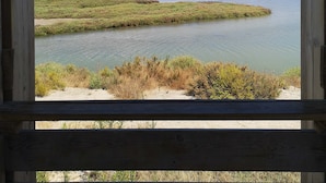 A view through a wooden-framed window of a calm body of water with grassy banks, under a clear sky. - House / Villa - Coma-ruga (Coma-Ruga)