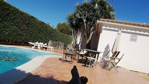 A poolside area with a tiled deck, lounge chairs, and a white building with a tiled roof. - House / Villa - Coma-ruga (Coma-Ruga)