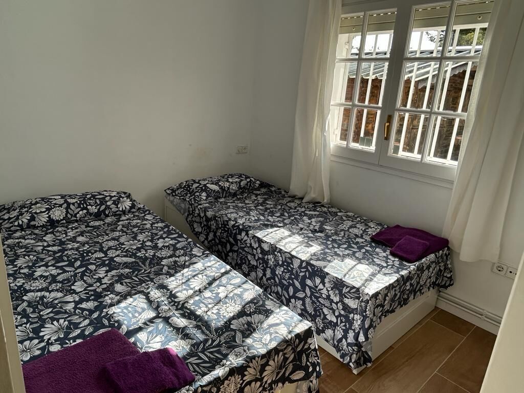 Une chambre avec deux lits, chacun recouvert d’une couvre-lit à motifs floraux, une fenêtre avec des volets blancs et un sol carrelé.