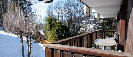 A wooden deck with a table and chairs, surrounded by snow and trees.
