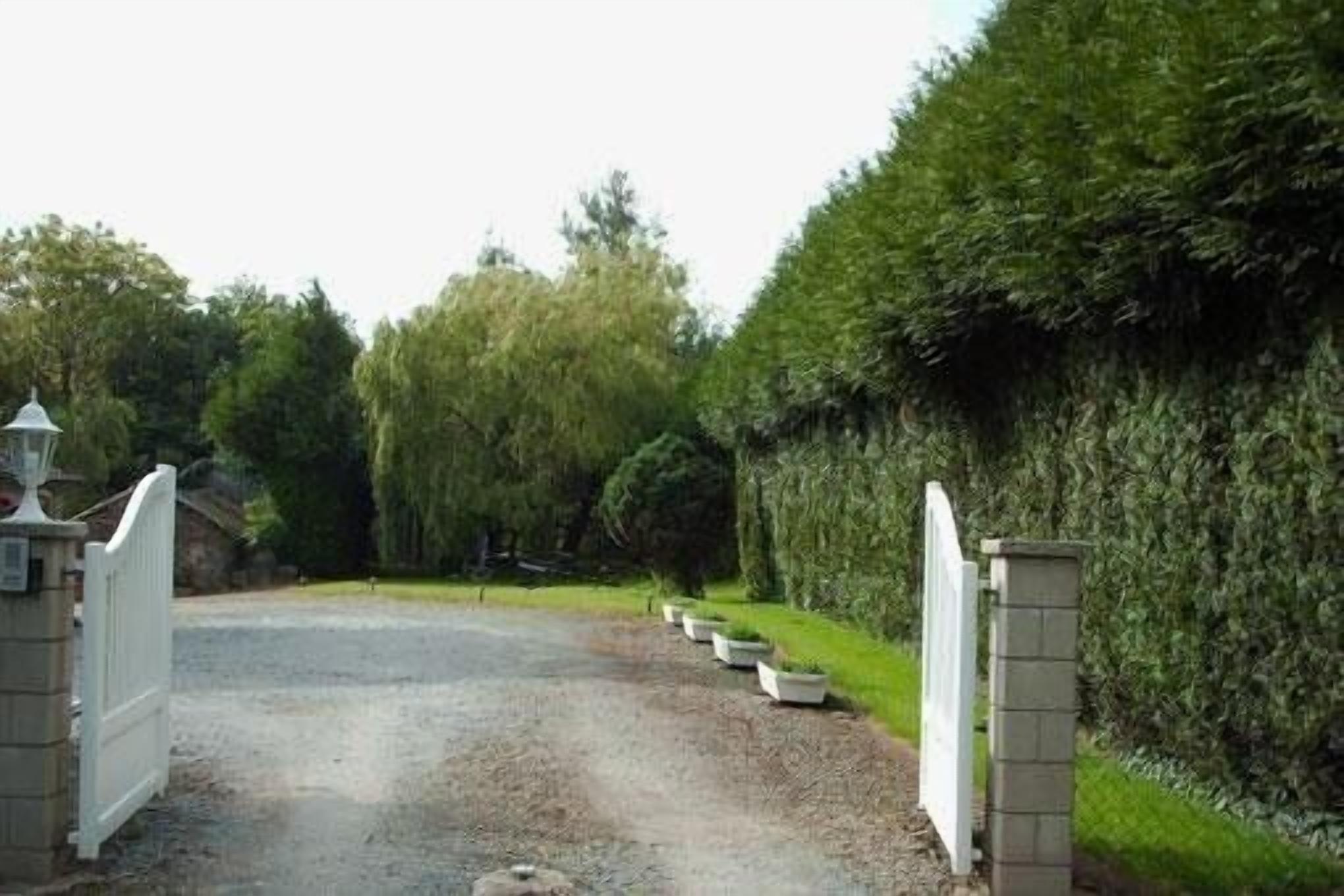A gravel driveway leading to a gated entrance with a white fence and a lamp post.