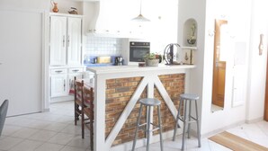 A kitchen with a white countertop, a brick accent wall, and two bar stools. - Former manor house, quiet estate, south courtyard and peaceful atmosphere (Evran)