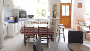 A bright kitchen with white cabinets, a stove, microwave, and a dining area with a table and chairs. - Former manor house, quiet estate, south courtyard and peaceful atmosphere (Evran)