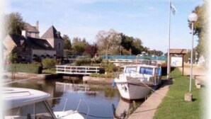 A canal with boats docked, a pedestrian bridge, and buildings in the background. - Former manor house, quiet estate, south courtyard and peaceful atmosphere (Evran)